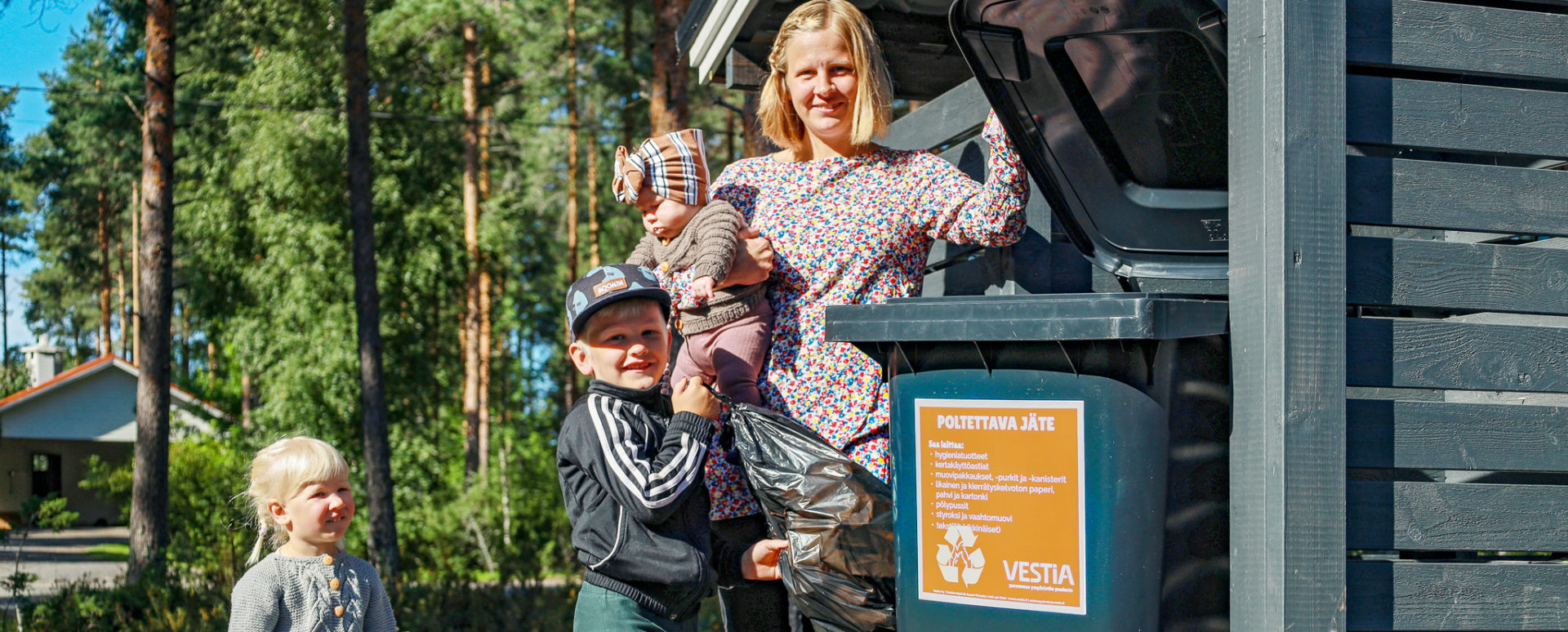 Äiti ja lapset viemässä roskapussia jäteastiaan.