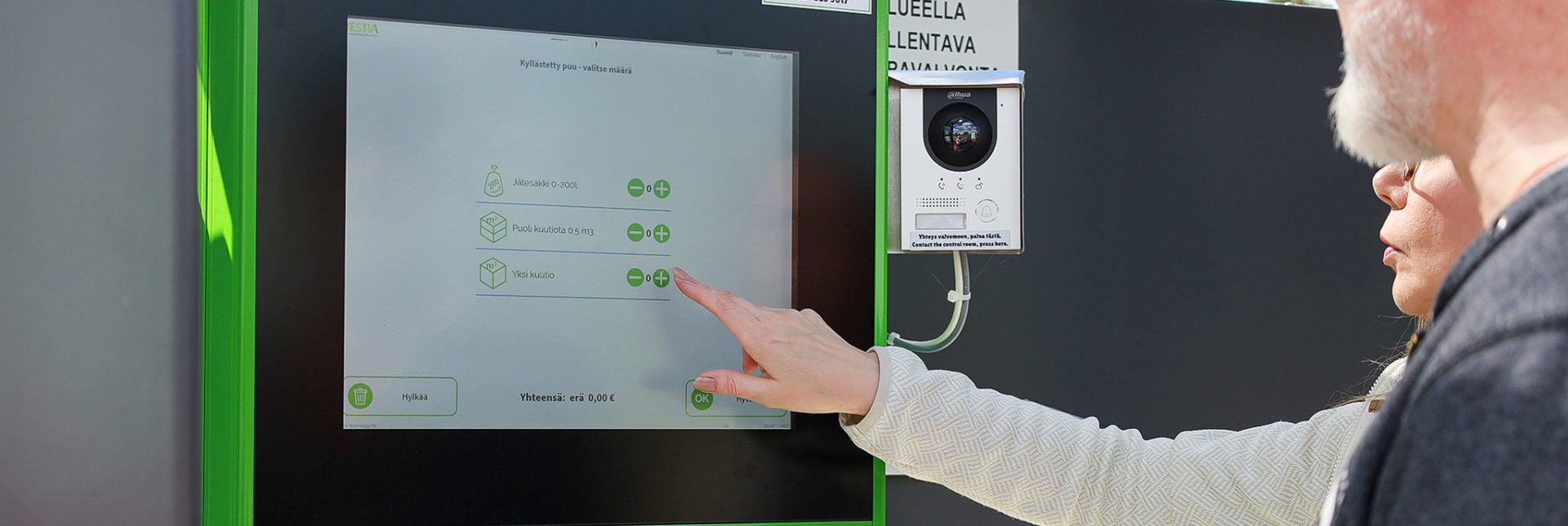 Maksuautomaatti Nainen ja mies ilmoittamassa jätekuormaa maksuautomaattiin