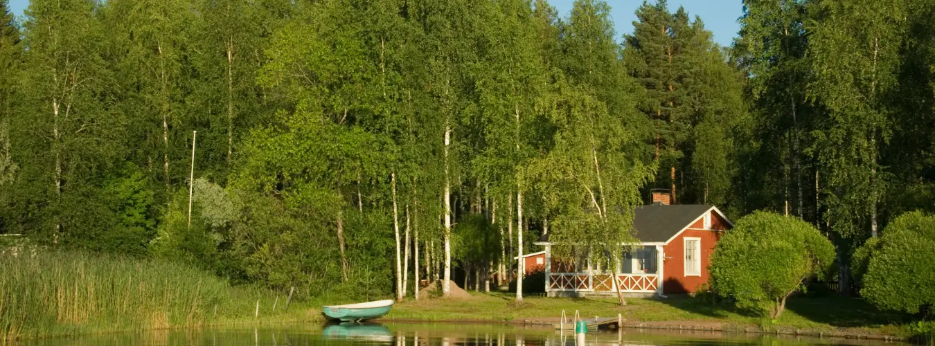 Veden rannalla oleva mökki. Artikkelin otsikko on Vapaa-ajan kiinteistöjen jätehuolto.