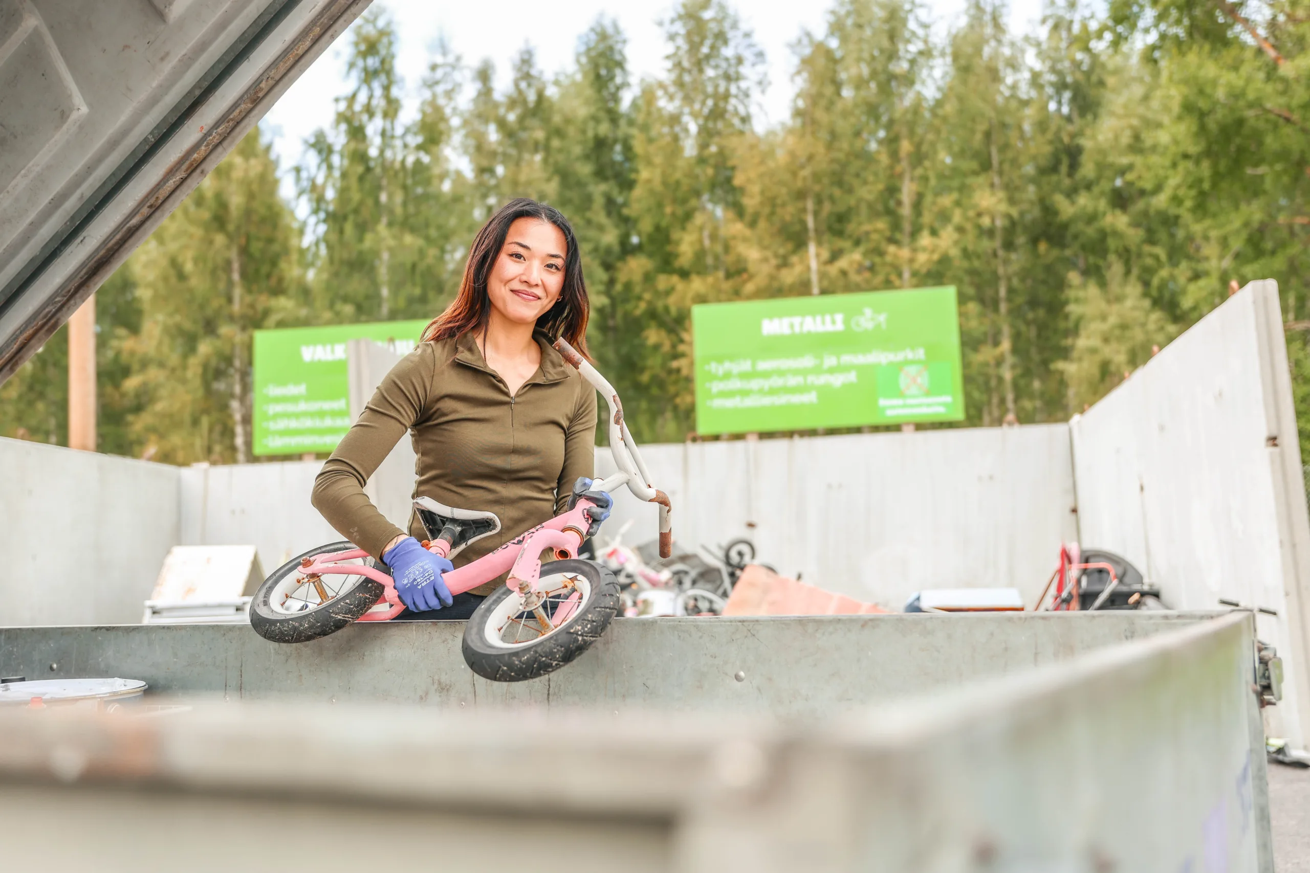 Henkilö lajittelupihalla nostamassa vanhaa lasten pyörää pois peräkärrystä