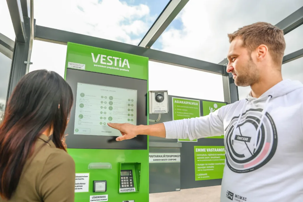 Kaksi henkilöä Vestian lajittelupihan itsepalveluautomaatilla ilmoittamassa jätteitä