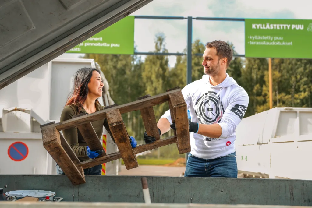 Kaksi henkilöä Vestian lajittelupihalla nostavat yhdessä puista lavaa pois peräkärrystä