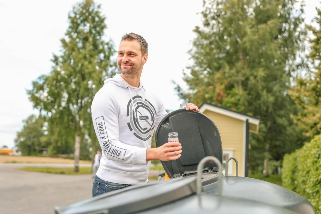 Henkilö ekopisteellä laittaa lasipurkkia lasinkeräysastiaan